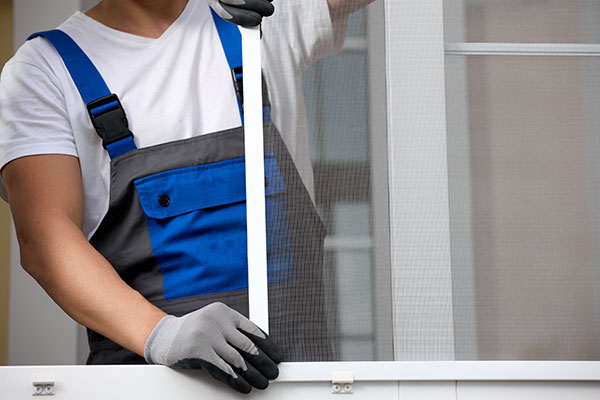 Handwerker passt ein Insektenschutzgitter in ein Fenster ein