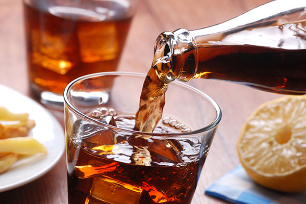 Cola wird aus einer Flasche in ein Glas mit Eiswürfeln gegossen