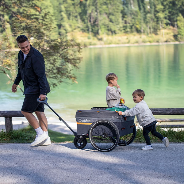 Vater mit zwei Kindern in einem Fahrradanhänger, Spaziergang am See