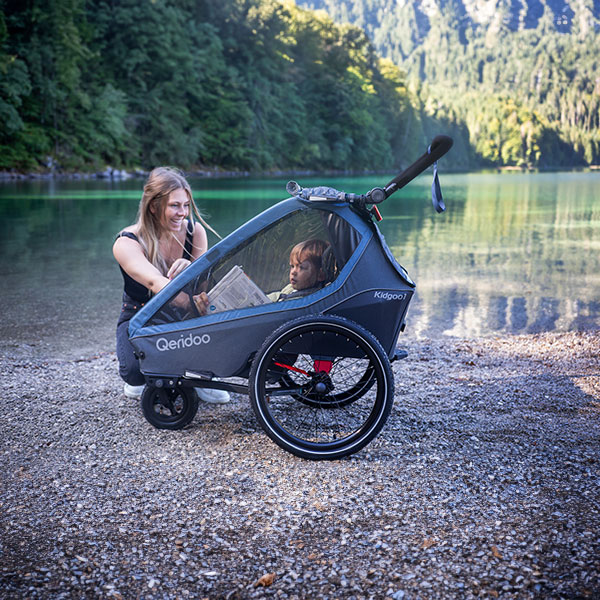 Frau mit Kind im Fahrradanhänger am Seeufer, idyllische Naturkulisse