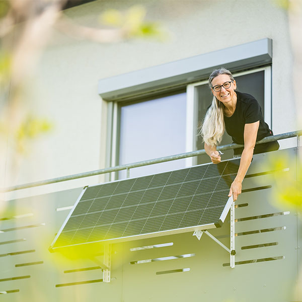 Frau installiert Solarmodul am Balkongeländer für ein Balkonkraftwerk