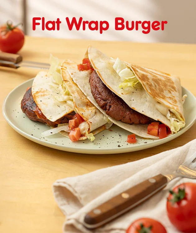 Auf dem Bild sieht man einen hellen Holztisch mit einem Teller, auf dem zwei halbierte Flat Wrap Burger liegen. Die Wraps sind goldbraun gebraten und gef&uuml;llt mit einer Fleischscheibe, Salat und gew&uuml;rfelten Tomaten. Die Burger sind leicht &uuml;bereinander auf einem hellgr&uuml;nen Teller angerichtet. Im Hintergrund liegt eine frische Tomate auf dem Tisch, daneben Besteck und ein gefaltetes Stofftuch. Oben im Bild steht in roter Schrift &bdquo;Flat Wrap Burger&ldquo;. Am unteren Rand befindet sich ein wei&szlig;er Button mit roter Umrandung und der Aufschrift &bdquo;Hier Rezept entdecken&ldquo;.