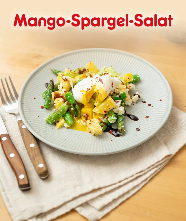 Motiv auf hellem Holztisch: &Uuml;berschrift &bdquo;Mango-Spargel-Salat&ldquo;. In der Mitte ein grauer Teller mit Mango‑Spargel‑Salat, dar&uuml;ber ein pochiertes Ei mit fl&uuml;ssigem Eigelb; dazu dunkle So&szlig;entropfen und Gew&uuml;rzflocken. Links liegen Messer und Gabel, rechts liegt eine gefaltete Serviette unter dem Teller. Unten ein Button &bdquo;Hier Rezept entdecken&ldquo;, der zum Klicken einl&auml;dt.