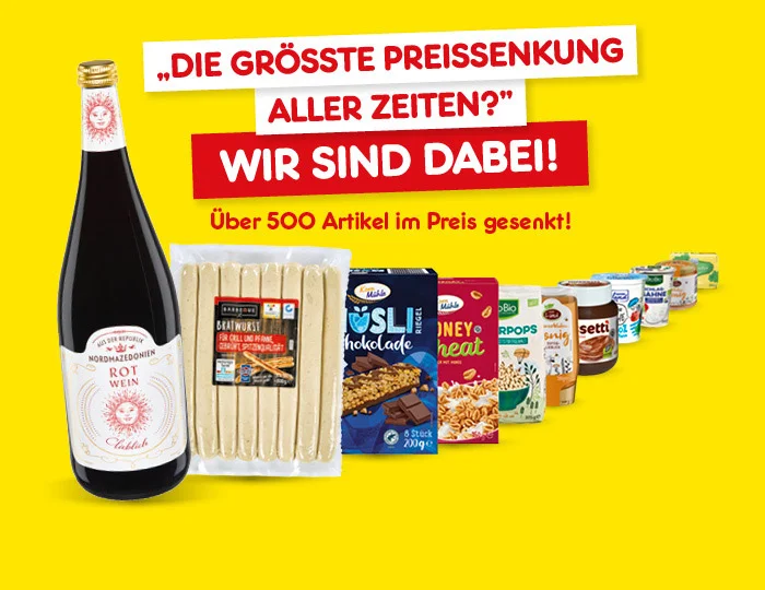 Bild zeigt eine Auswahl von Produkten vor einem gelben Hintergrund. Oben steht der Text "DIE GR&Ouml;SSTE PREISSENKUNG ALLER ZEITEN? WIR SIND DABEI! &Uuml;ber 500 Artikel im Preis gesenkt!". Zu sehen sind eine Flasche Rotwein, eine Packung Spargel, M&uuml;sli, Schokolade und weitere Lebensmittel. Unten befindet sich ein Button mit der Aufschrift "Preisgesenkte Angebote entdecken".